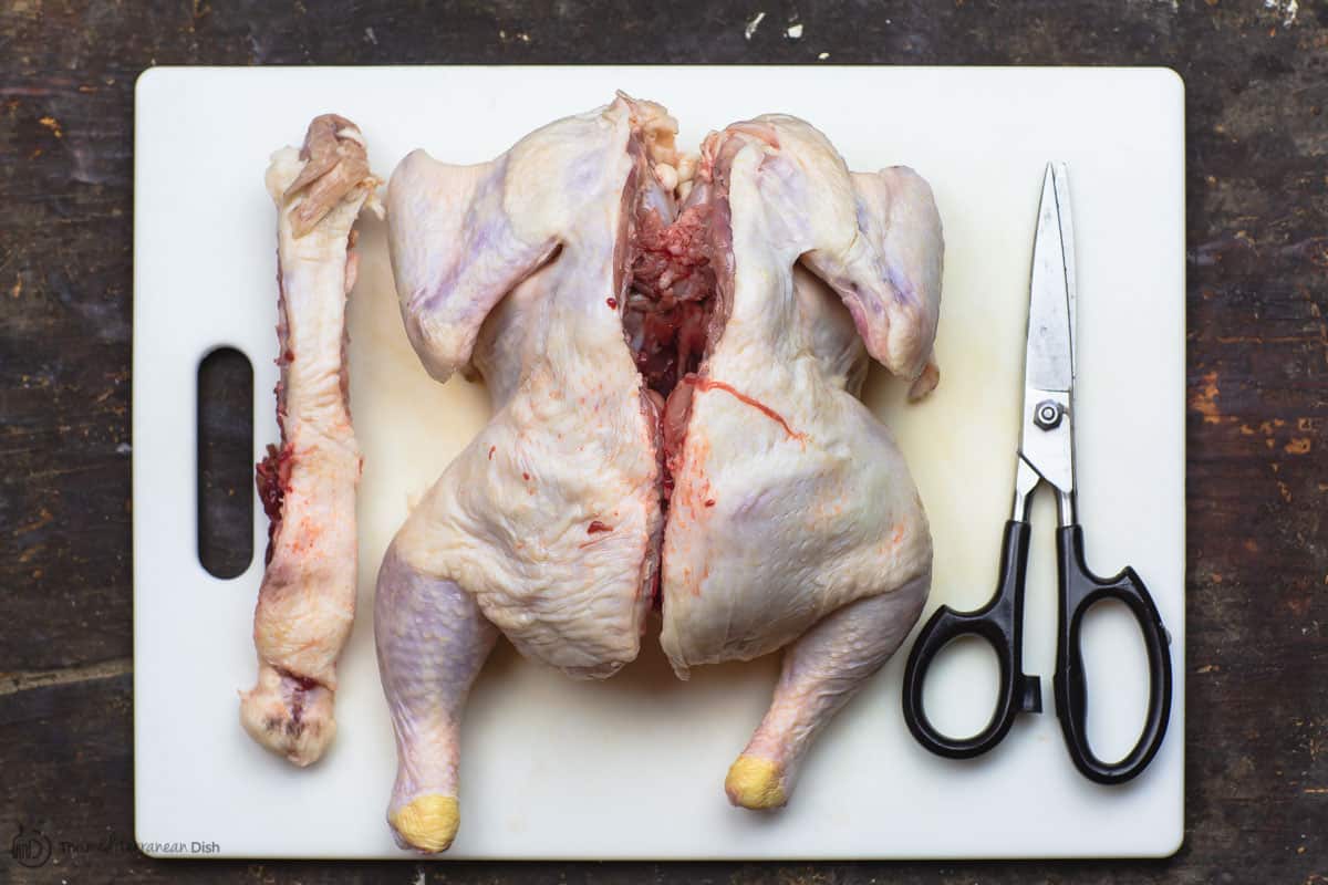 Whole chicken with spine cut out and laid on cutting board