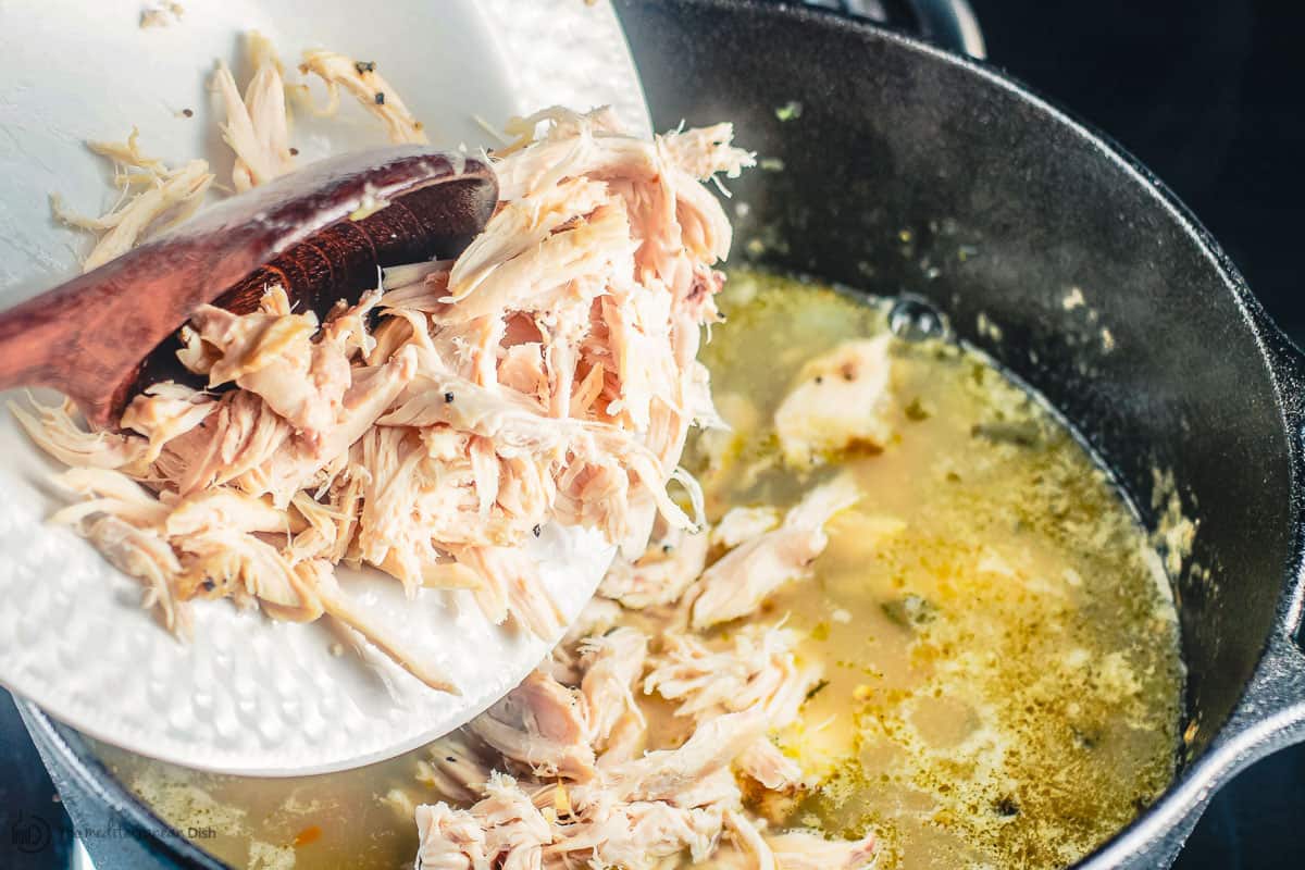 Cooked shredded chicken being added to pot of broth and rice 