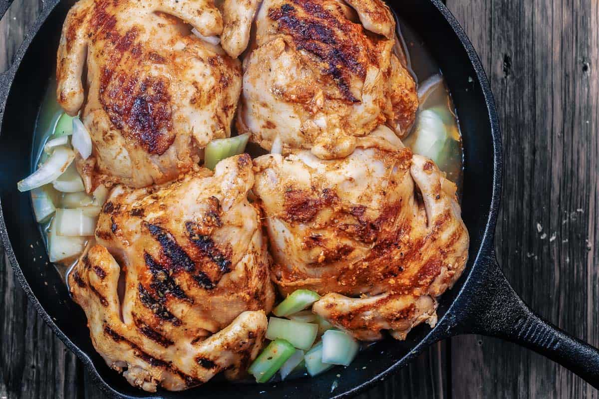 Cornish hen placed in cast iron skillet with onions and celery