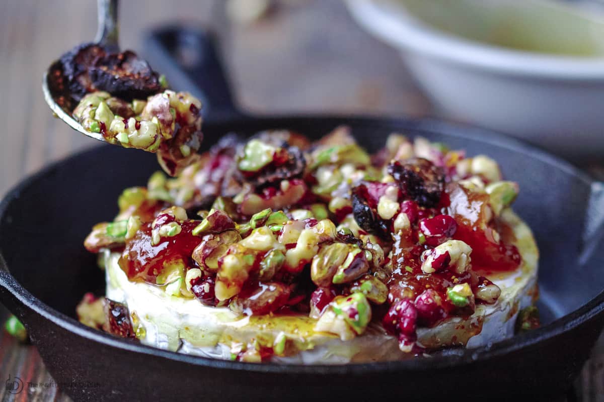 Toppings being spread on top of brie wheel