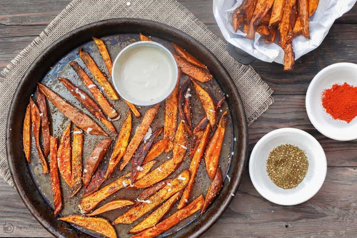 Sweet potato fries in baking sheet with spices and tahini