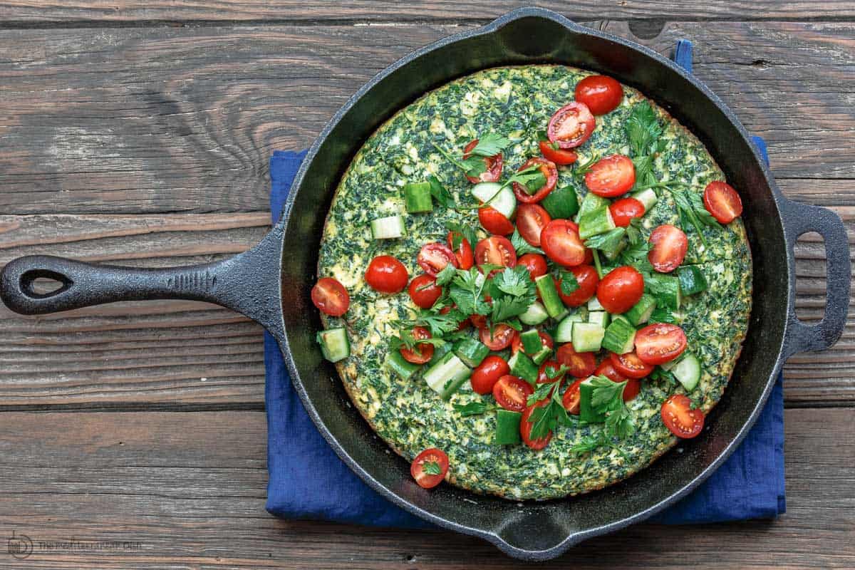 Skillet with cooked spinach firttata. Bright Mediterranean salad served on top