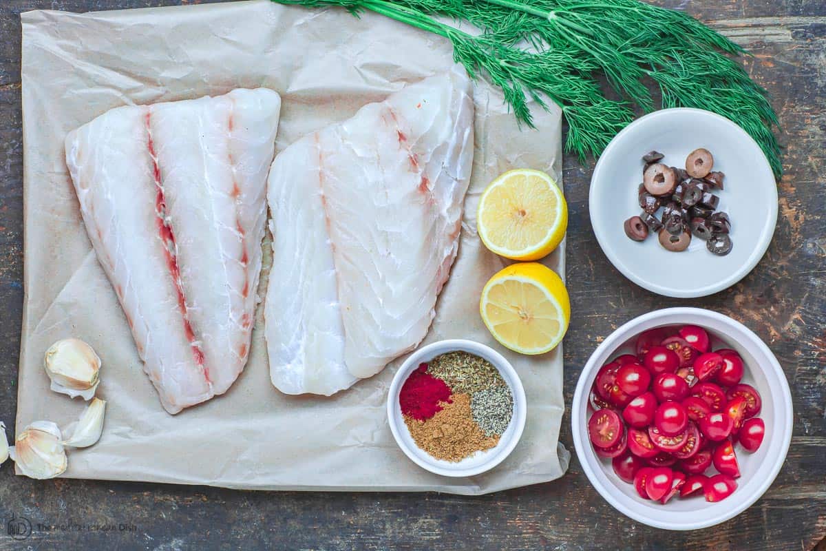 Ingredients for baked grouper recipe. Fish, spices, tomatoes, olives, fresh dill, and lemon juice