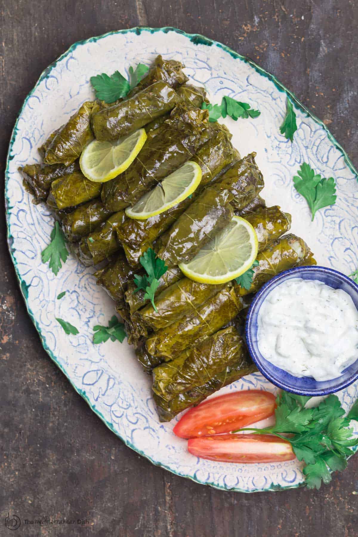 Stuffed Grape Leaves (Dolmas) on serving platter with tztaziki sauce and sliced tomatoes