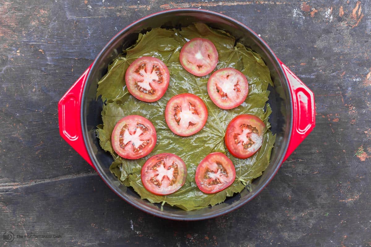 Cooking pot with sliced tomatoes on top of layer of open grape leaves