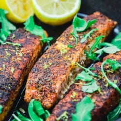 crispy pan seared salmon in a cast iron pan with lemon halves and arugula