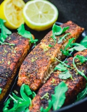 crispy pan seared salmon in a cast iron pan with lemon halves and arugula