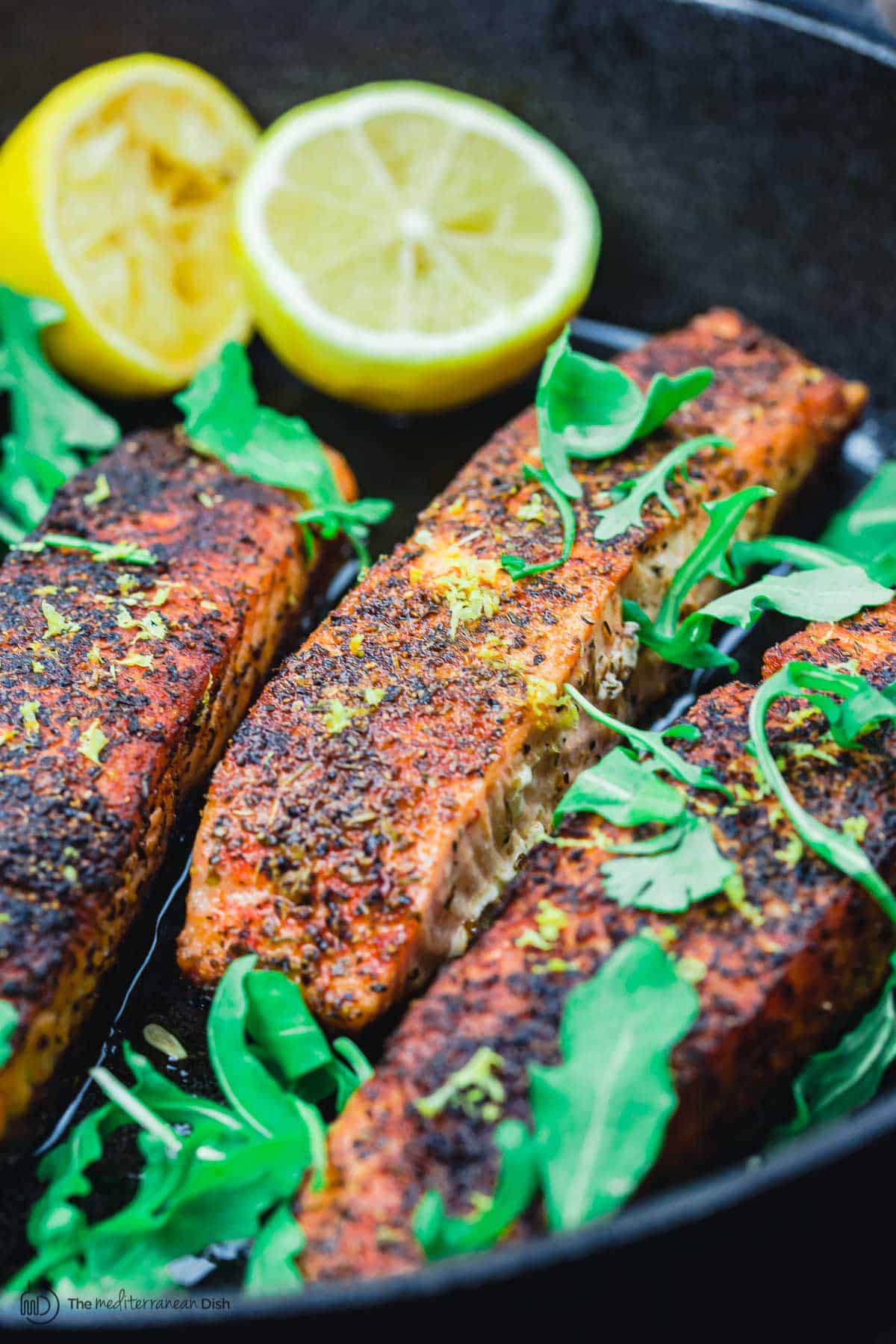 crispy pan seared salmon in a cast iron pan with lemon halves and arugula