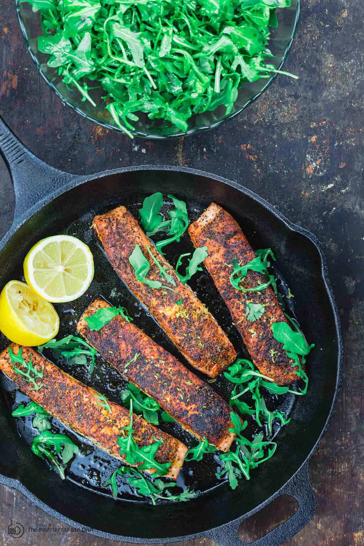 Salmón frito en la sartén y una guarnición de rúcula