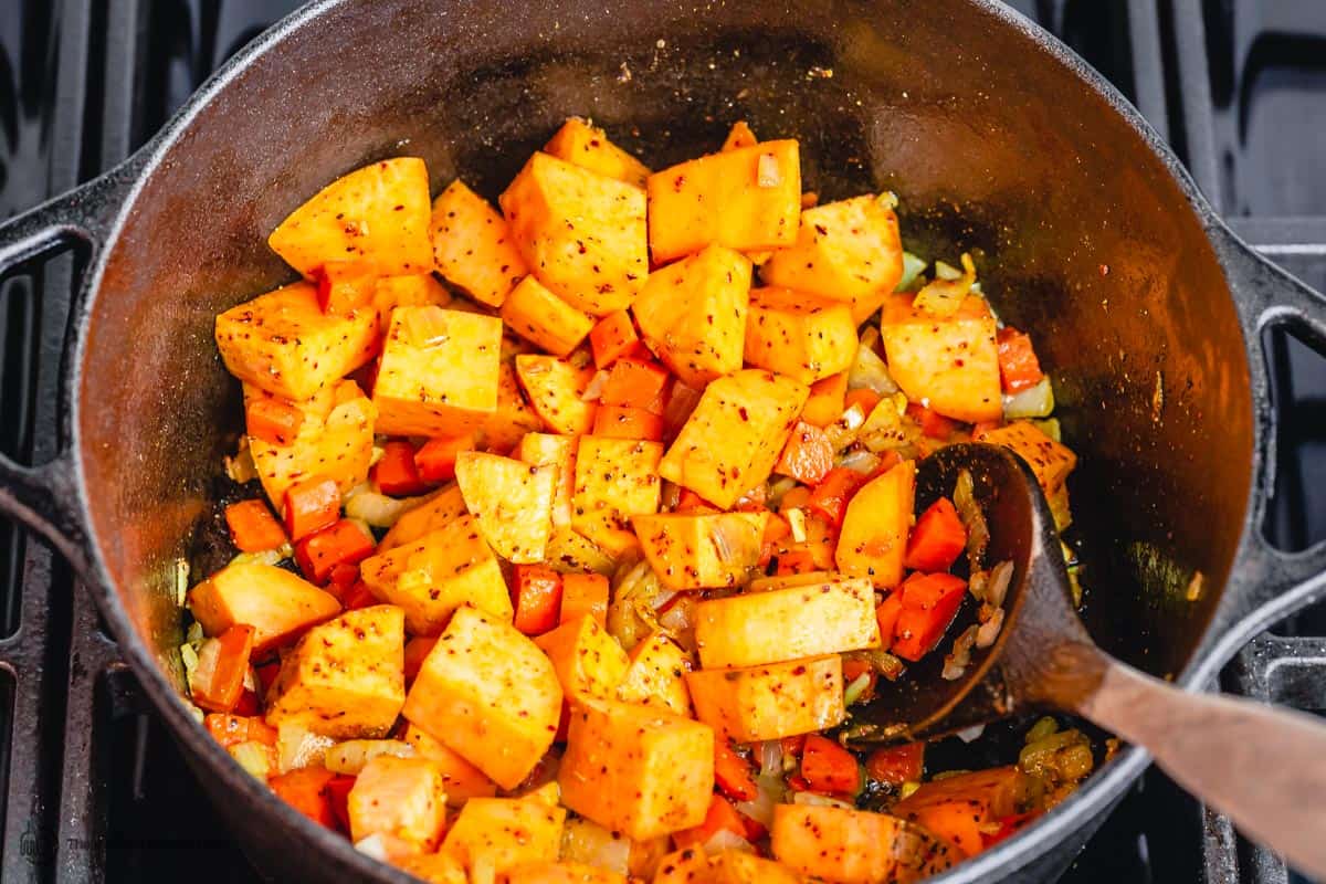 Sweet potatoes being sauteed with carrots, onions, and garlic