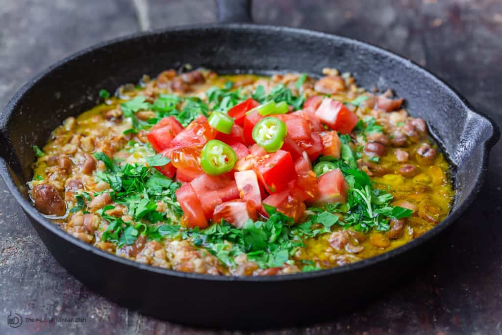 Ful medammas topped with fresh parsley, tomatoes, and a few slices of hot chili peppers