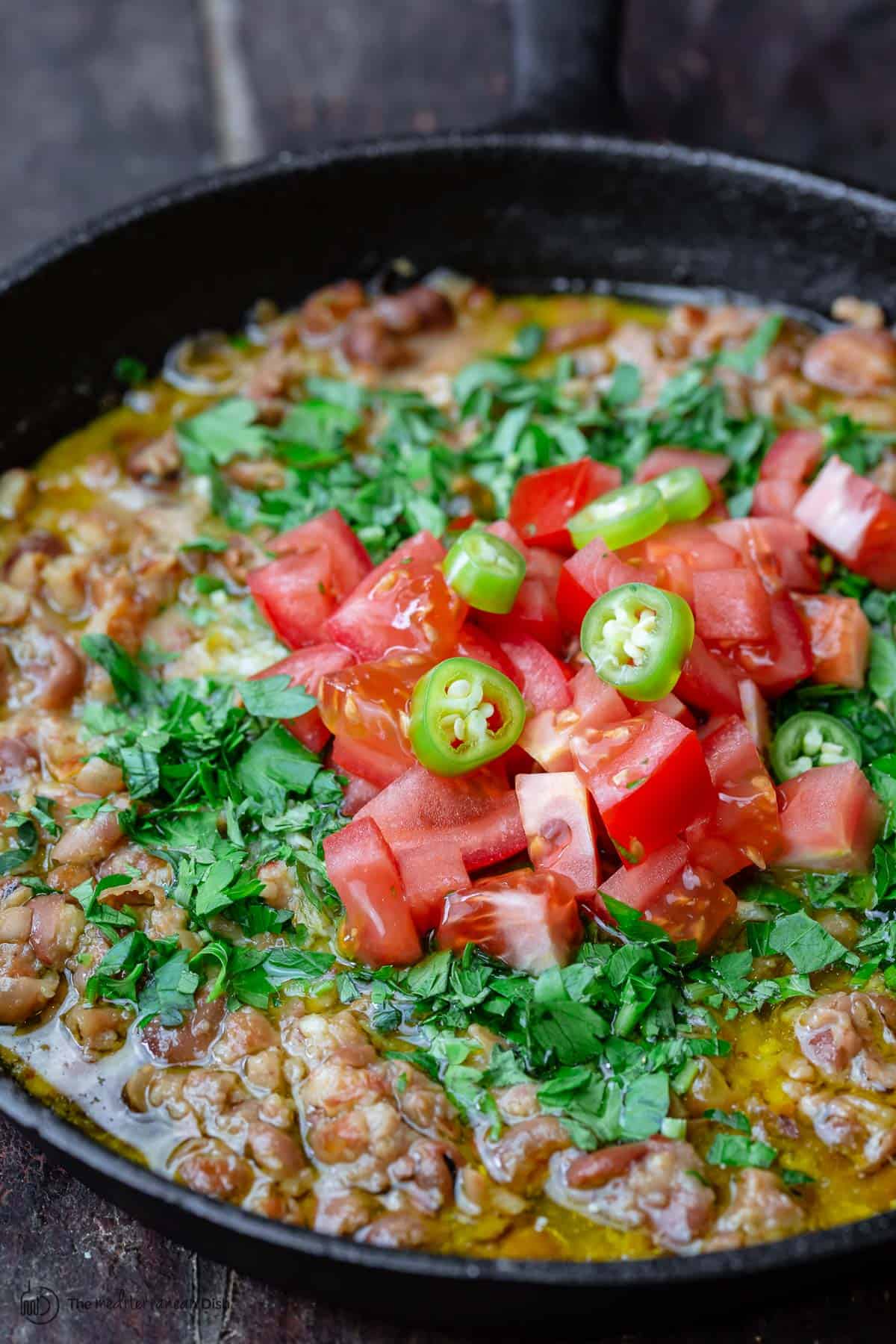ful medames in skillet, topped with fresh tomatoes and parsley
