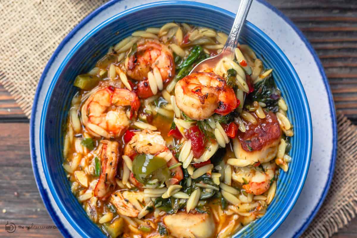 shrimp soup with orzo, vegetables, spinach and fresh herbs, served in blue dinner bowl