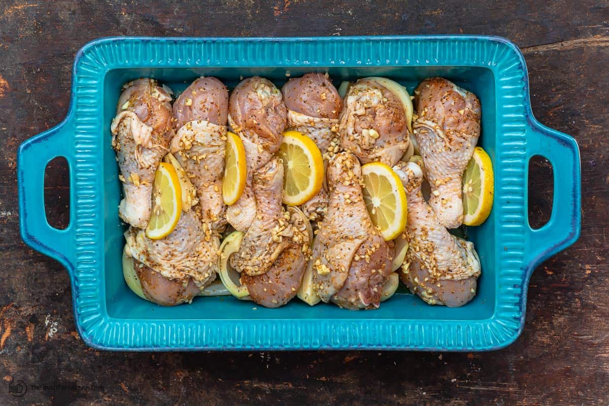 raw chicken drumsticks and lemon slices arranged in baking dish