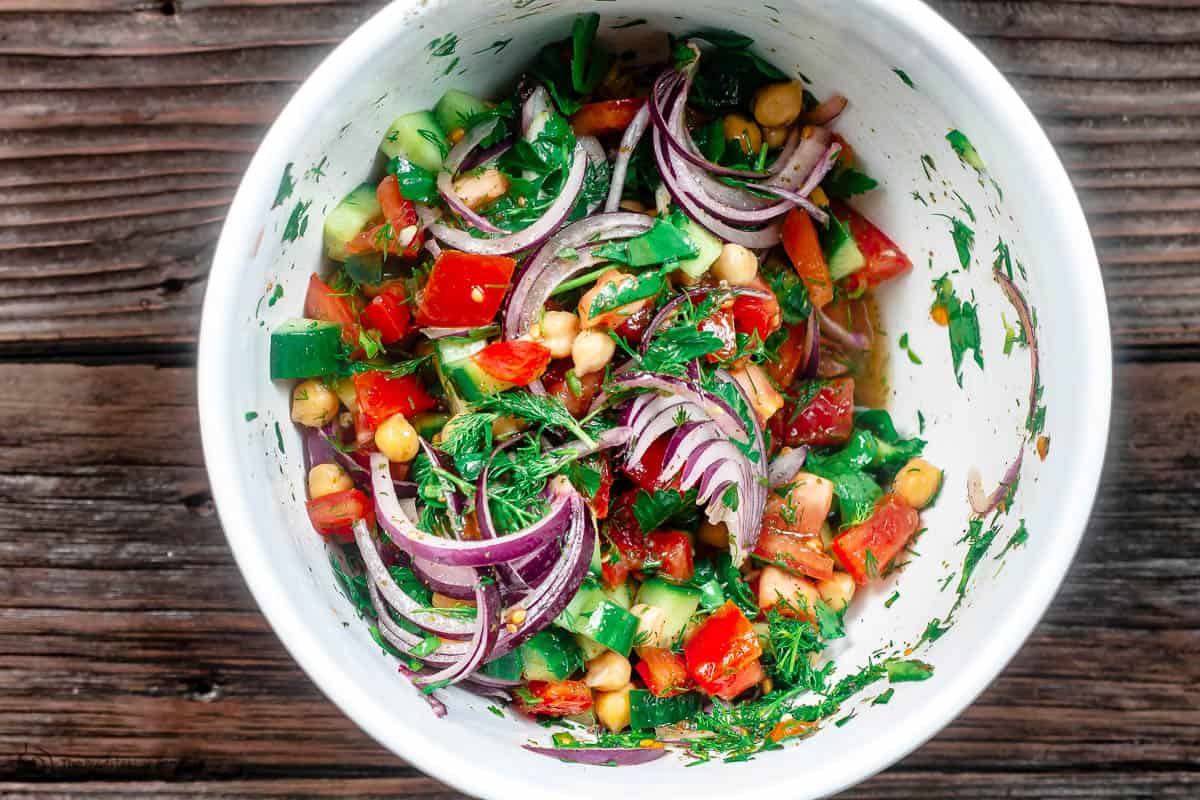 chickpea salad tossed with veggies and herbs in mixing bowl