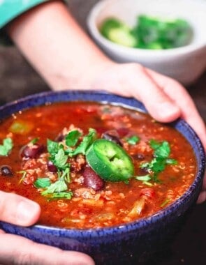 Bowl of vegan chili being held with a pair of hands