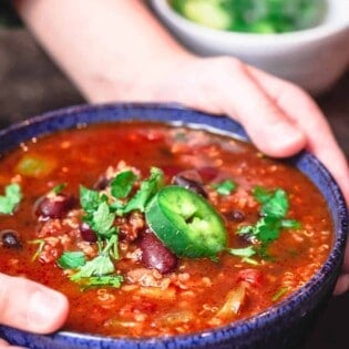 Bowl of vegan chili being held with a pair of hands