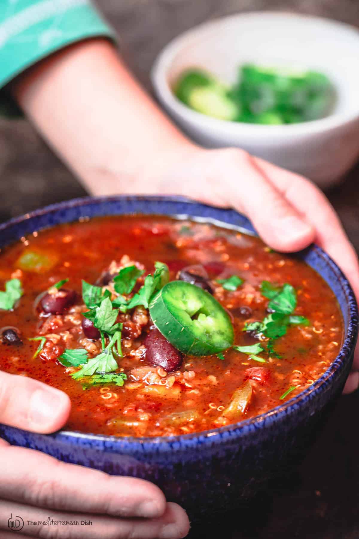 Bowl of vegan chili being held with a pair of hands