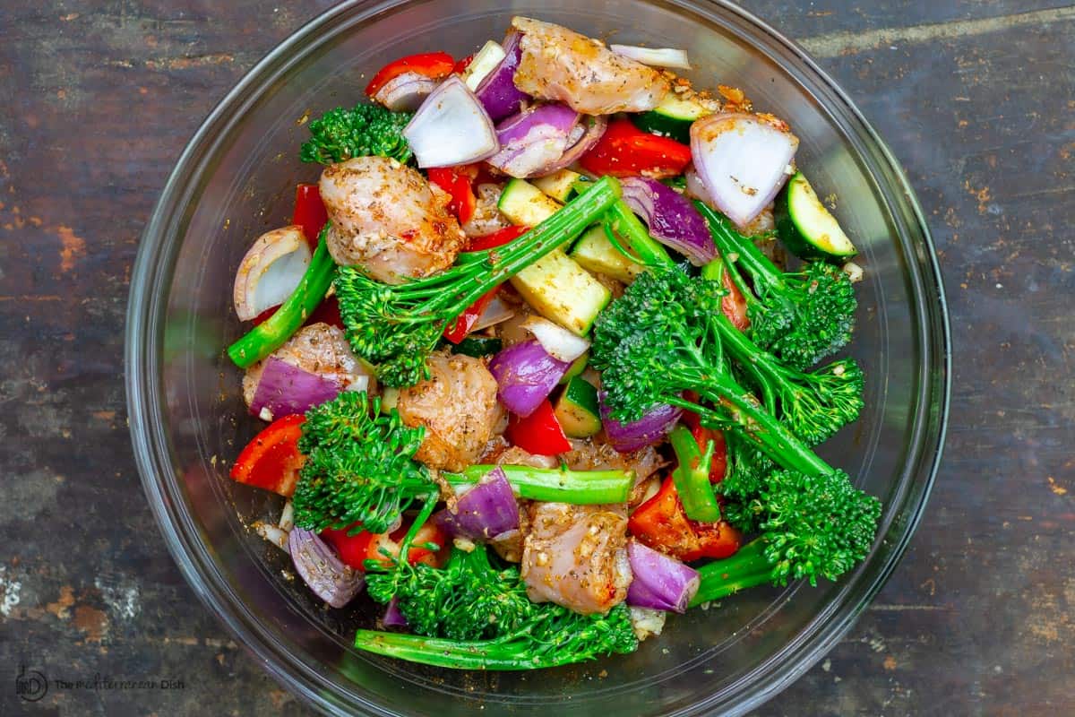 Chicken and vegetables in a bowl, tossed with garlic and spices and olive oil