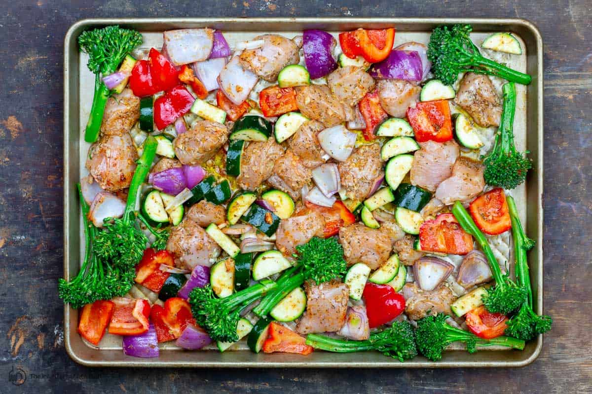 Chicken and vegetables arranged on a large sheet pan and ready to bake