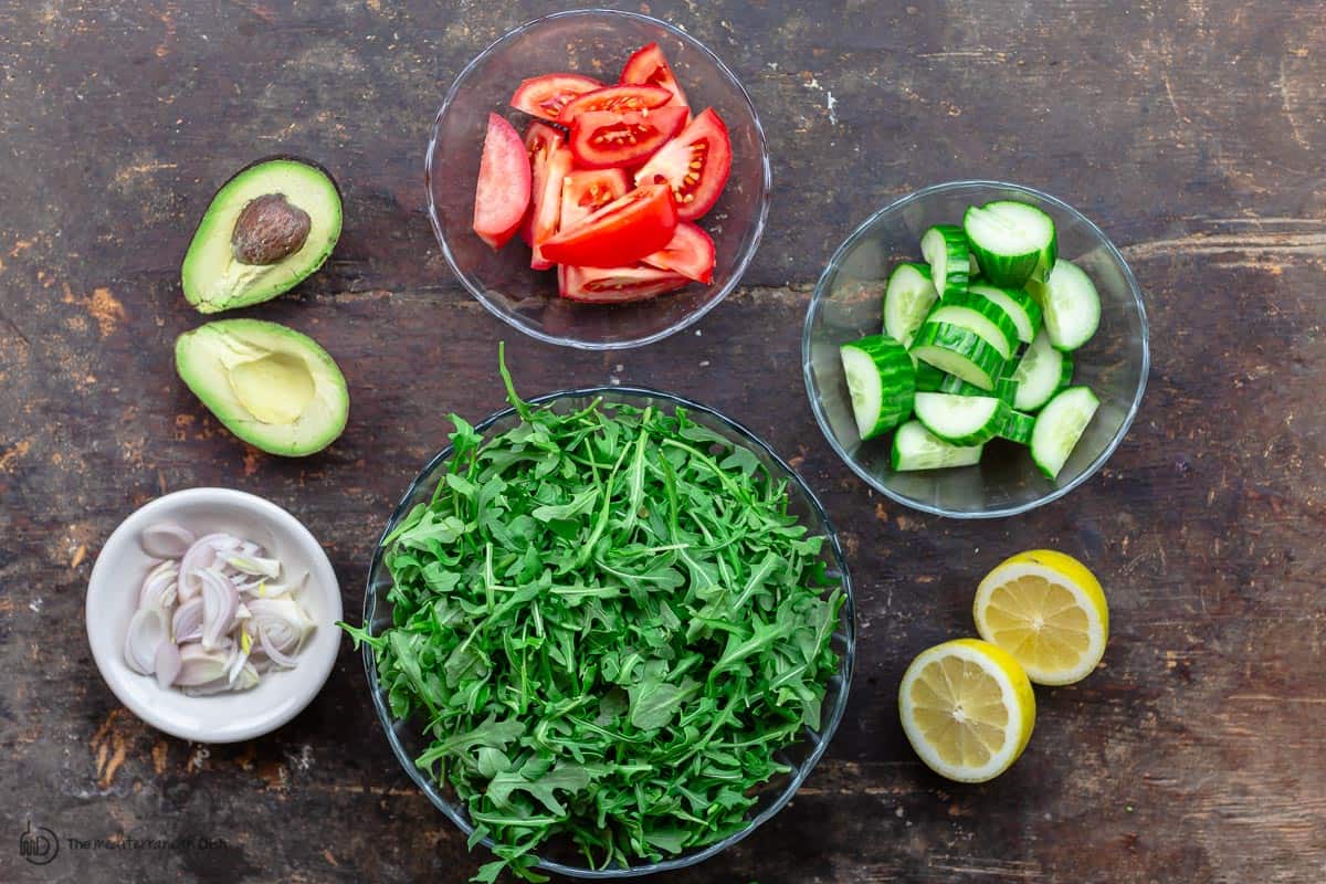 Arugula salad ingredients. Arugula, cucumber, tomatoes, shallots, and avocado