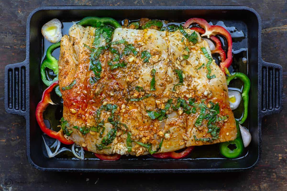 Fish fillet placed in baking pan with marinade, shallots and bell peppers