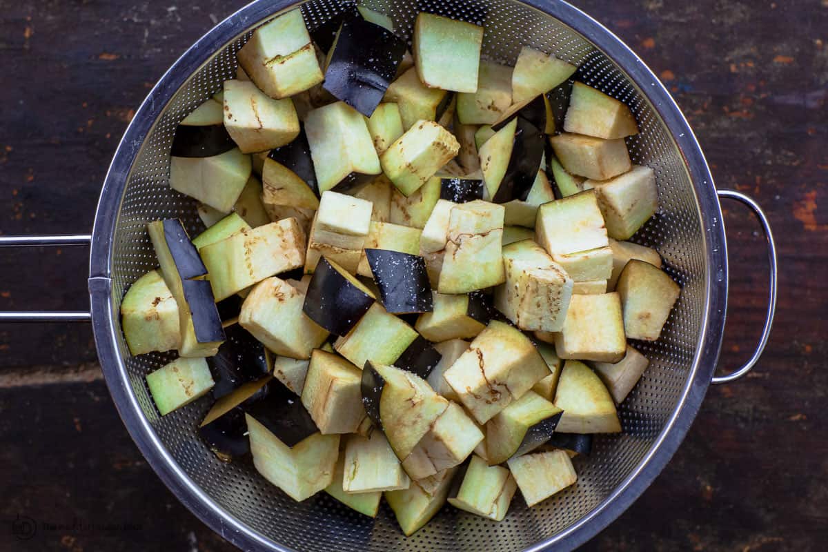 Salted cubed eggplant in a large colander 