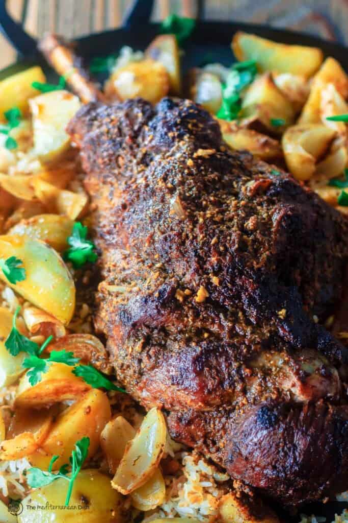 roast leg of lamb with potatoes on platter over a bed of rice