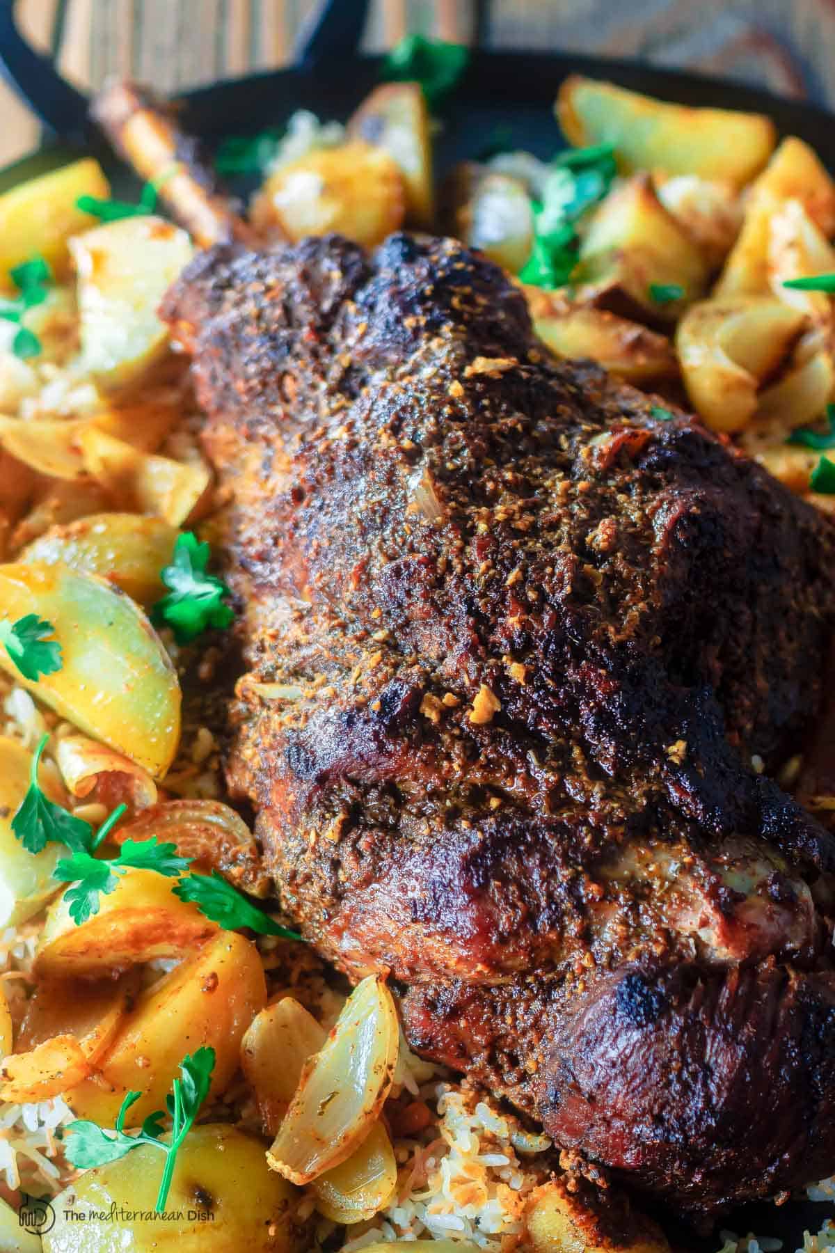 Roast leg of lamb with potatoes on platter over a bed of rice