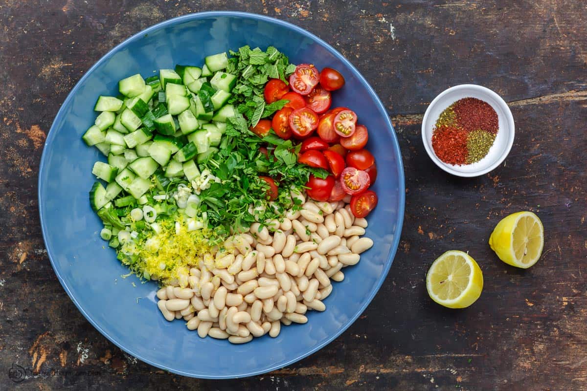 White beans, vegetables, fresh herbs in a big bowl. A small dish of spices and lemon to the side