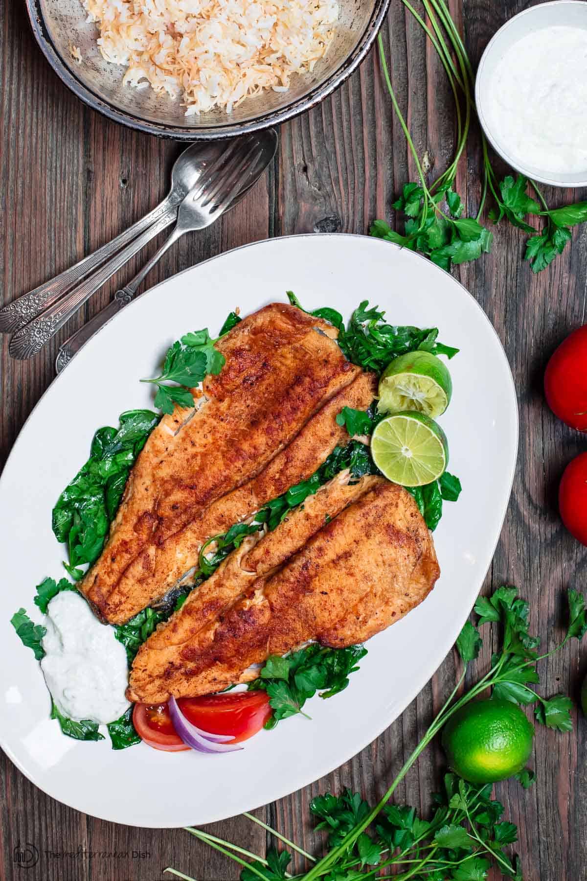 Seared rainbow trout served with a side of lebanese rice, limes, and tztaziki sauce