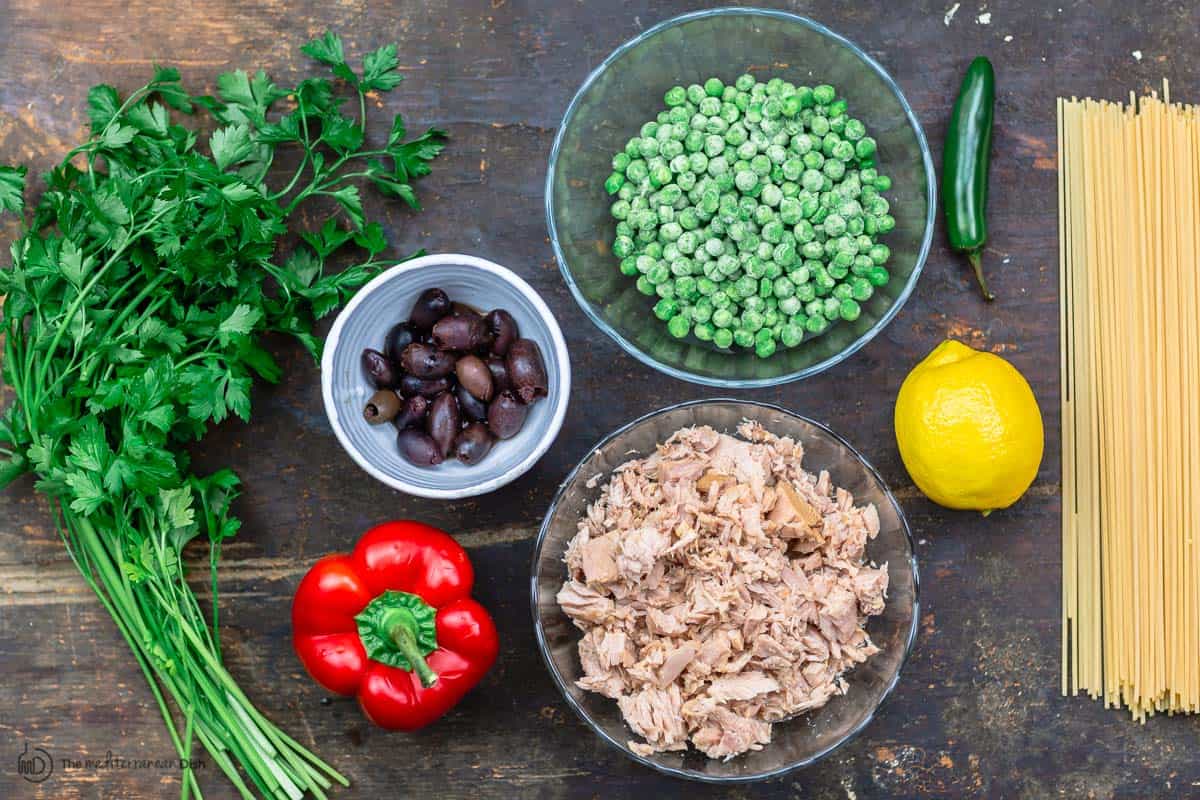 ingredients for tuna pasta. spaghetti, tuna, lemon, frozen peas, bell pepper, olives, parsley and jalapeno