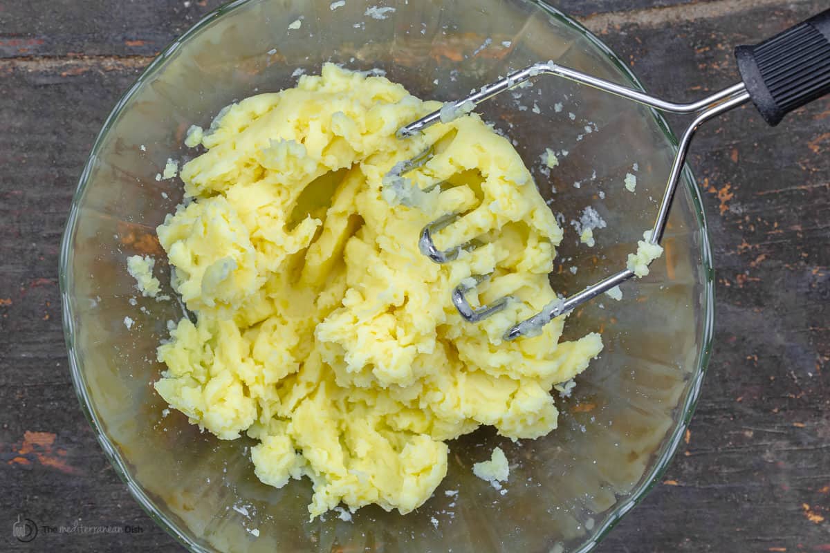 Potatoes being mashed with a masher in a bowl