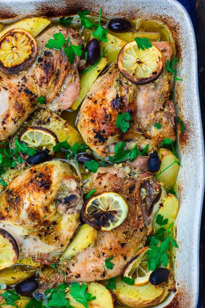Greek chicken and potatoes garnished with parsley, olives and lemon slices
