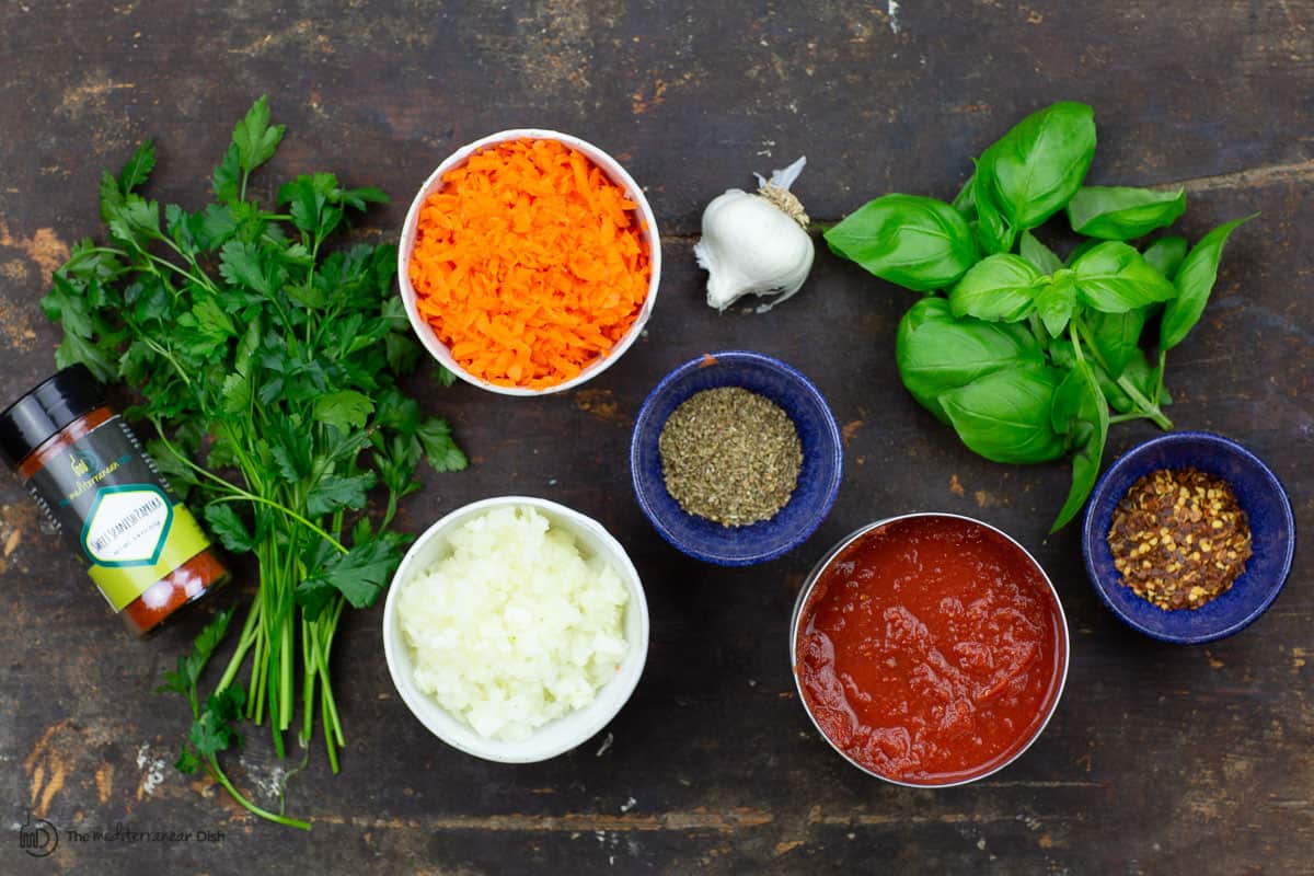 Ingredients for homemade spaghetti sauce: onions, garlic, carrots, canned crushed tomatoes, spices, and fresh herbs