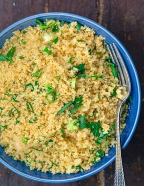 Cooked couscous in serving bowl, garnished with fresh herbs