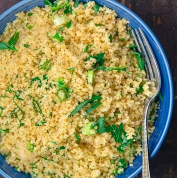 Cooked couscous in serving bowl, garnished with fresh herbs