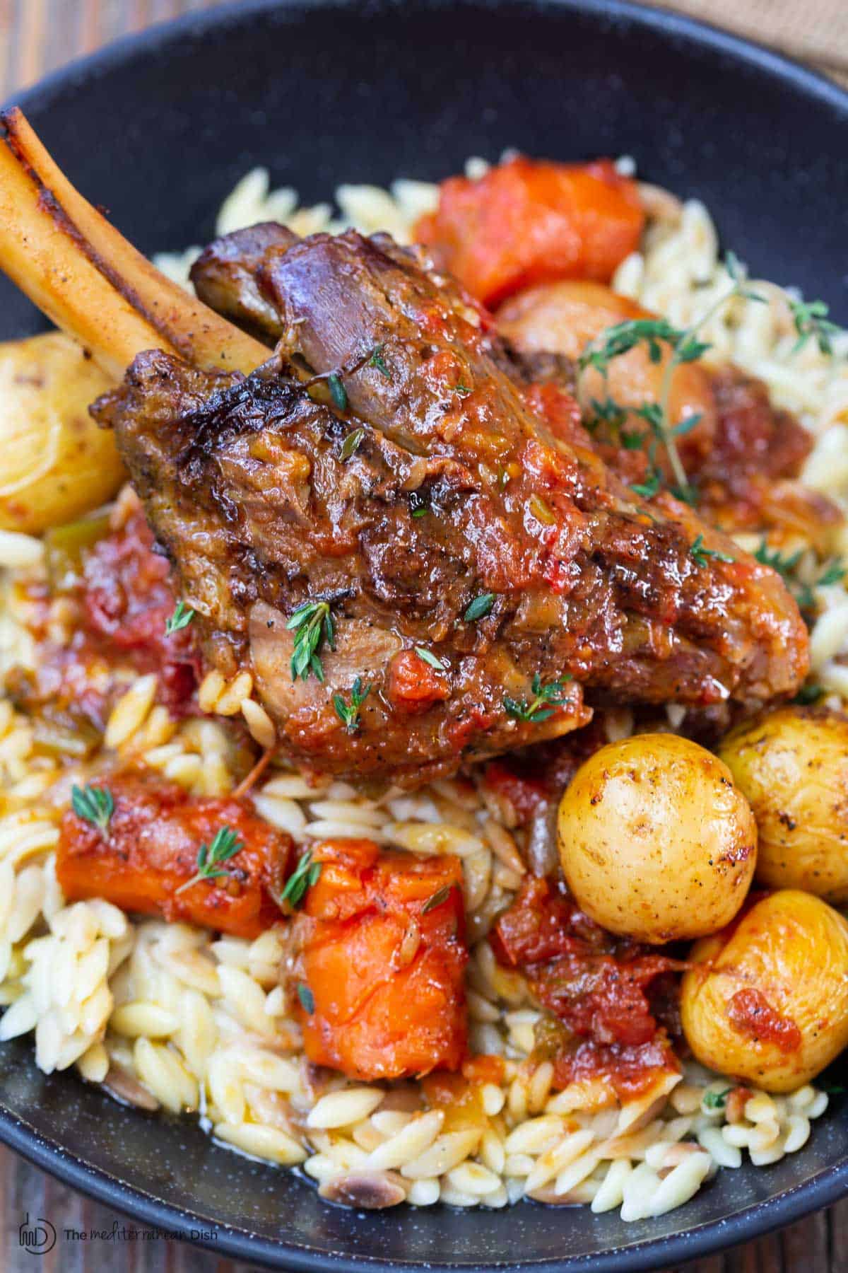 one lamb shank served with vegetables and orzo