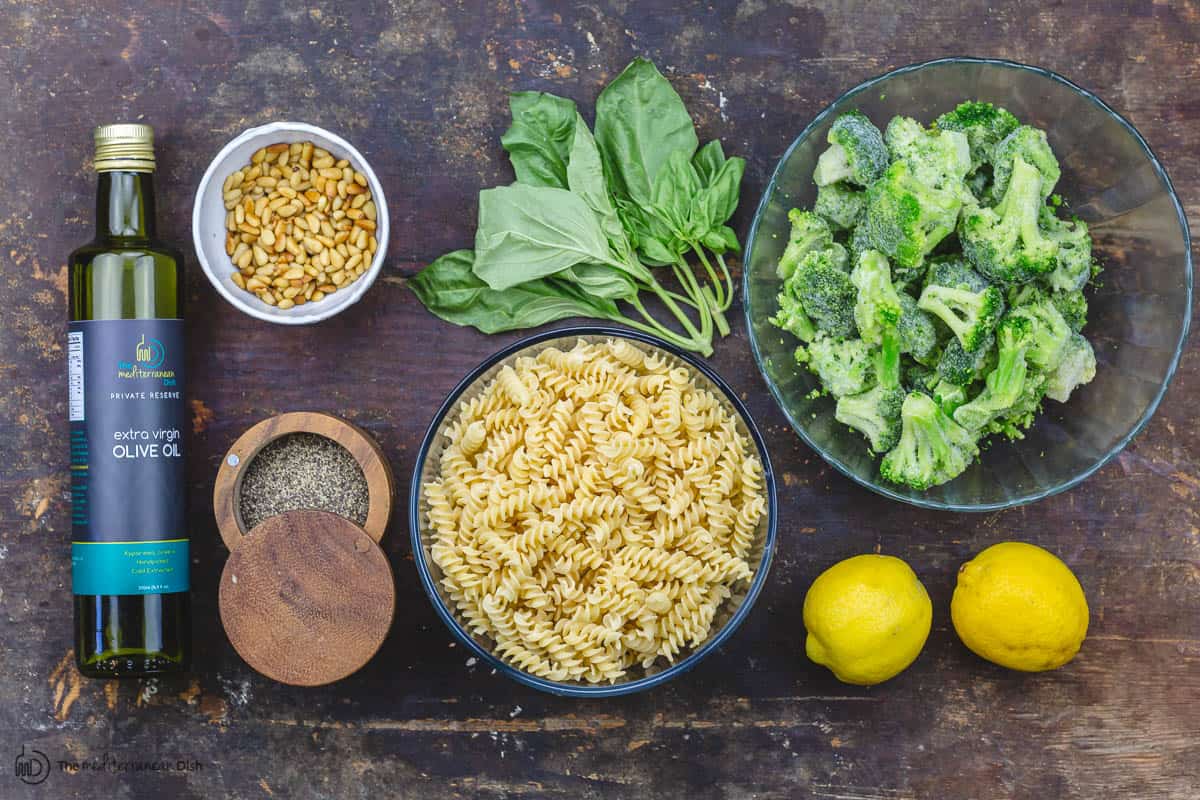 ingredients for pesto pasta: pasta, broccoli, lemon, basil leaves, pine nuts, pepper, parmesan cheese, olive oil 