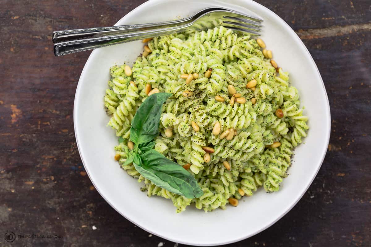 Pesto pasta served in a bowl with forks and fresh basil for garnish