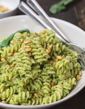 lemon broccoli pesto pasta served in dinner bowl. A side of pine nuts and fresh basil