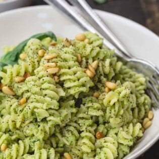 lemon broccoli pesto pasta served in dinner bowl. A side of pine nuts and fresh basil