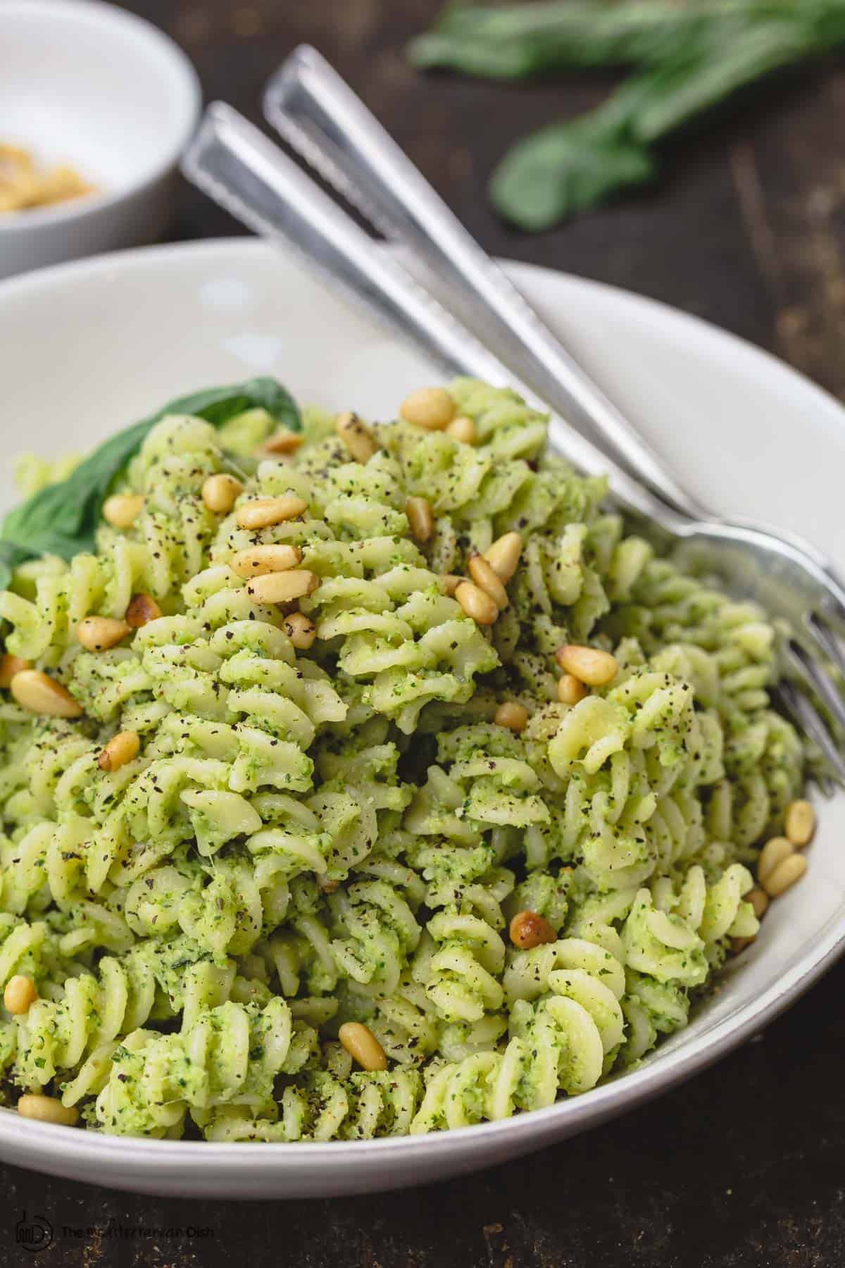 lemon broccoli pesto pasta served in dinner bowl. A side of pine nuts and fresh basil