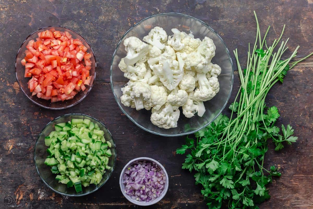 ingredients including caulfilower, tomatoes, cucumber, parsley, and red onions