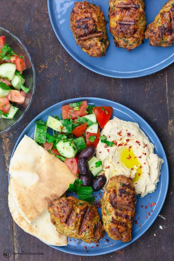 Two plates of chicken kofta patties with a side salad and hummus