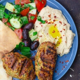 two chicken kofta with hummus, salad and pita on blue plate for serving