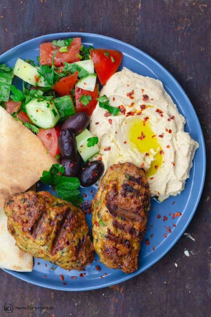 two chicken kofta with hummus, salad and pita on blue plate for serving