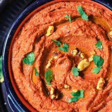 Muhammara roasted red pepper and walnut dip in a bowl, topped with walnuts and parsley for garnish