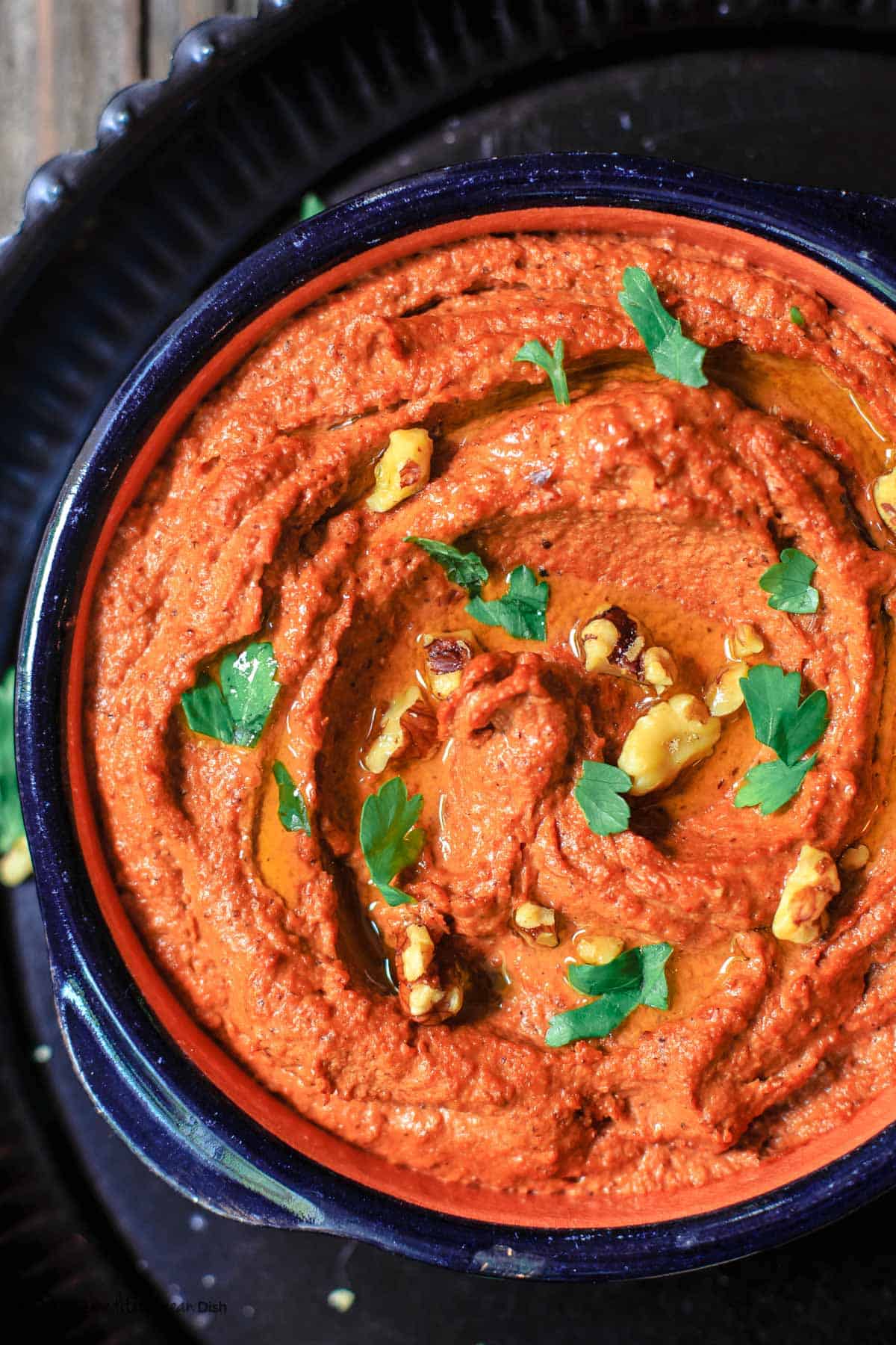 Muhammara roasted red pepper and walnut dip in a bowl, topped with walnuts and parsley for garnish