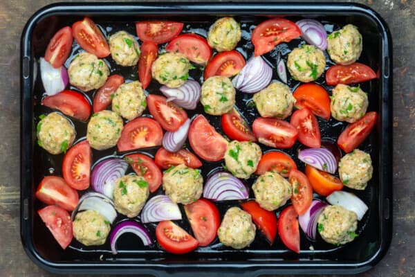 chicken meatballs arranged with tomatoes and onions on sheet pan before baking